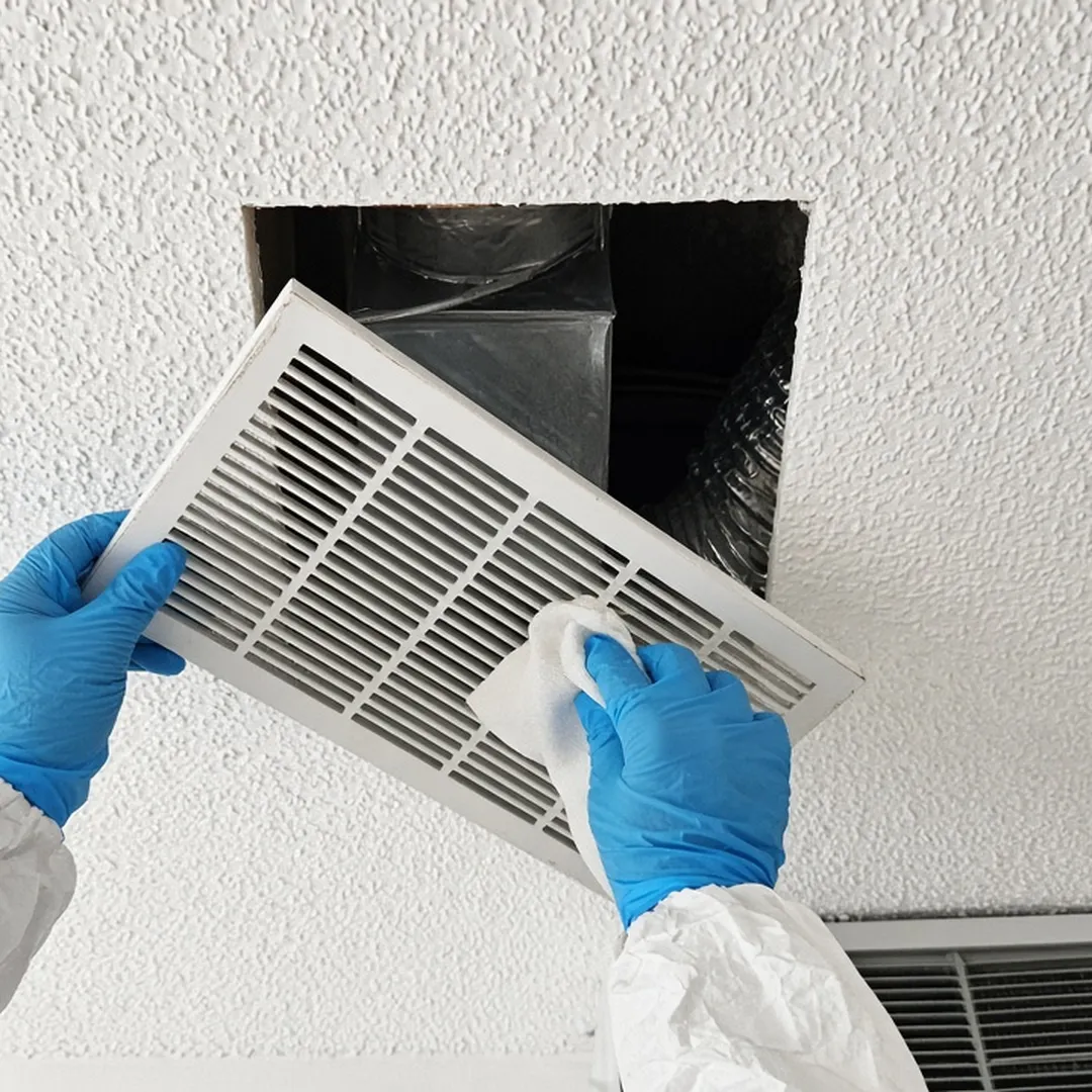 Gloved hands cleaning a ceiling air vent in an Arlington home during odor removal after a death